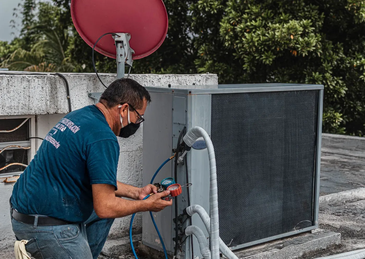 A technician reading a set of gauges connected to an outdoor air conditioning unit.