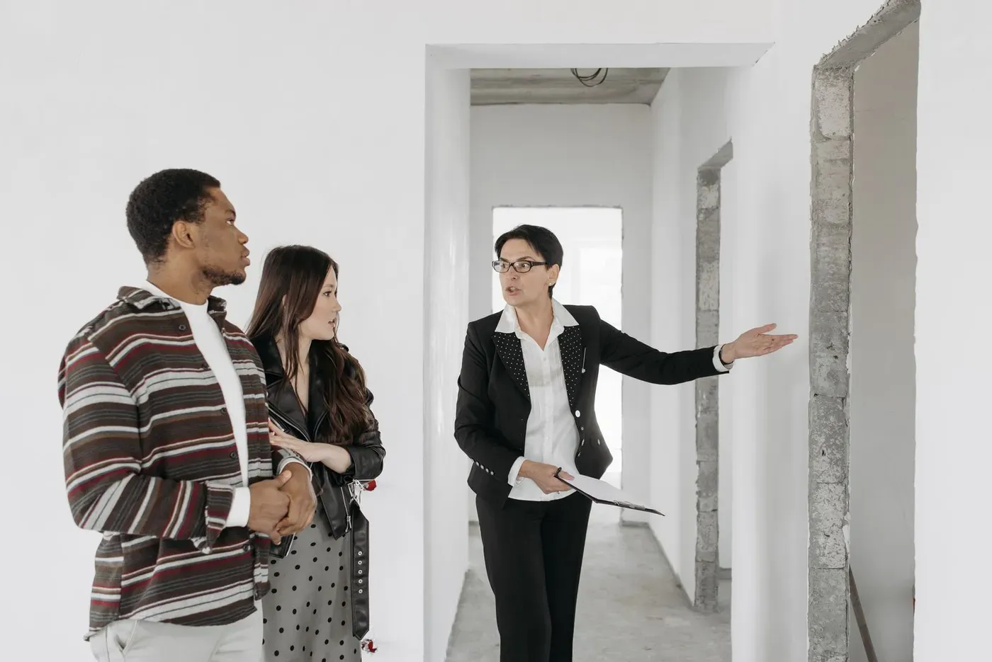 An agent in a dark suit showing an unfinished interior to a couple.