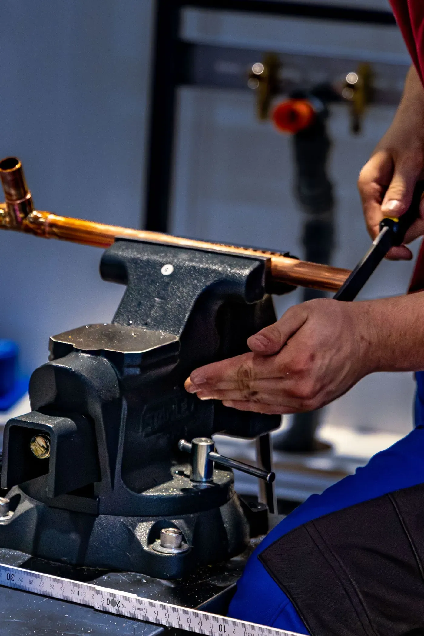 Hands working on a length of copper pipe held in a bench vise.