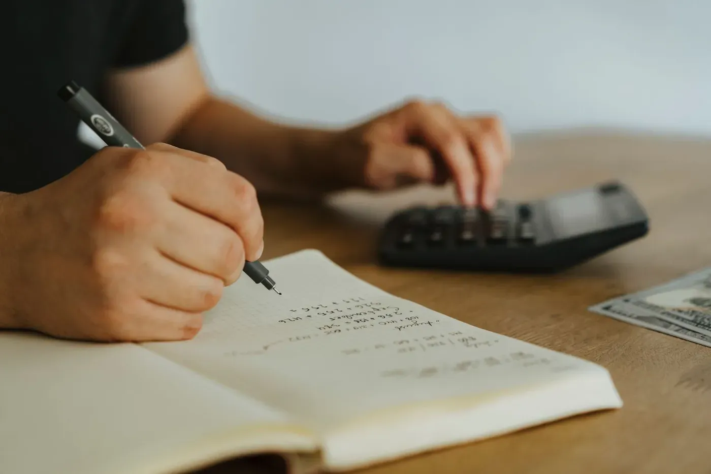 Hands writing figures in a notebook beside a calculator.