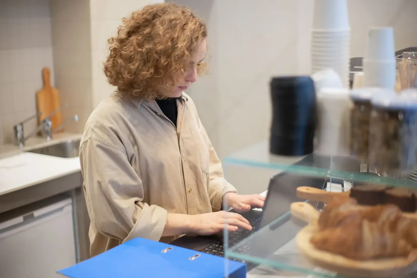 A café owner typing on a laptop behind a counter of pastries.