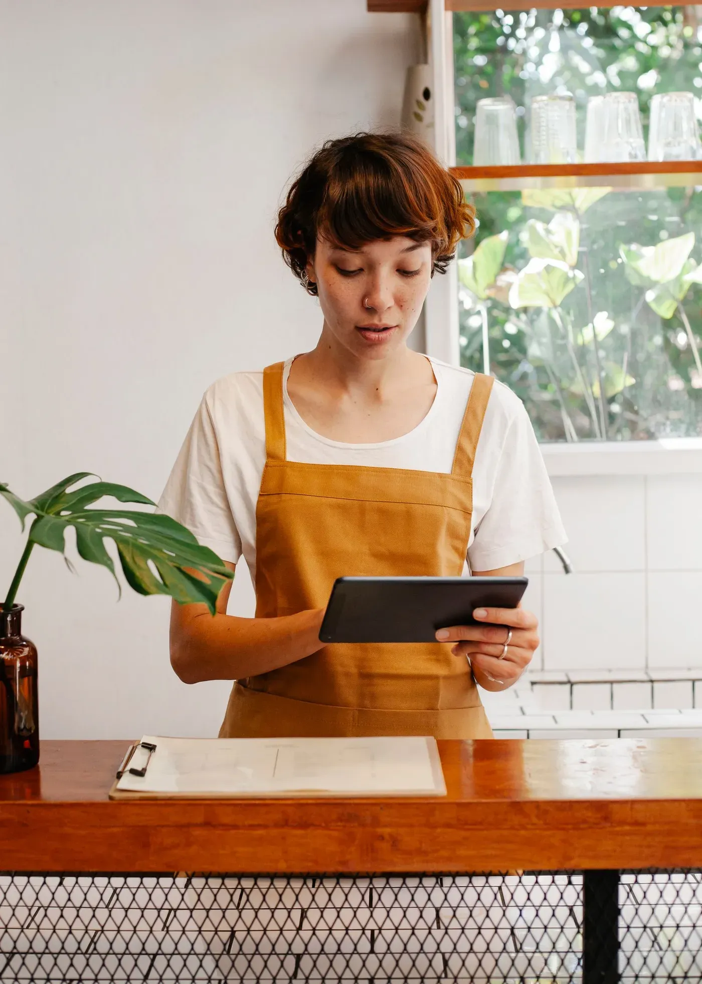 A cafe worker in an apron checking a tablet behind the counter.