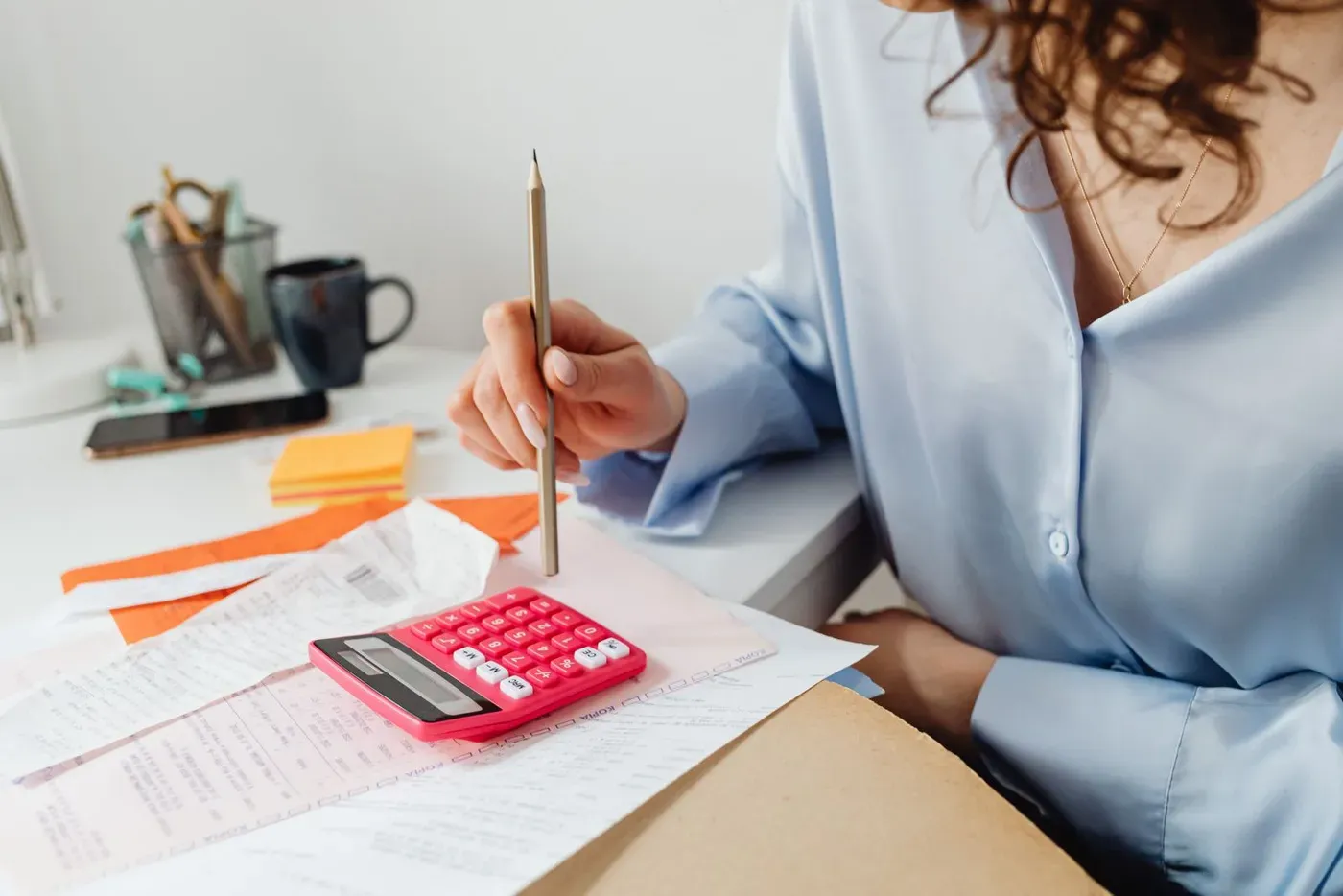 A woman working out expenses with a calculator and receipts at a desk.