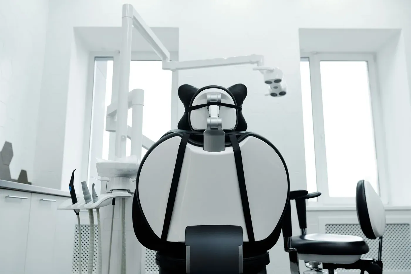 An empty dental chair in a bright white treatment room with two windows.