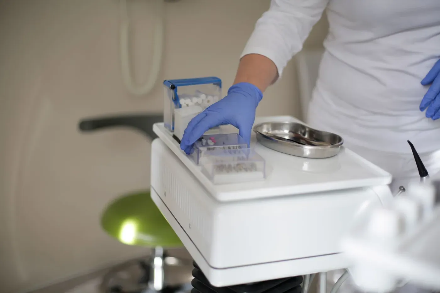 A gloved hand reaching for a box of dental burs on a white instrument stand.