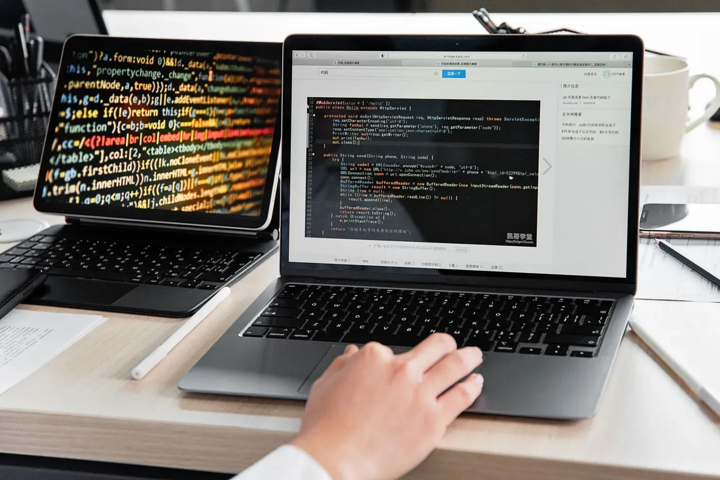 A developer typing code on a laptop, with a second screen full of code beside it.