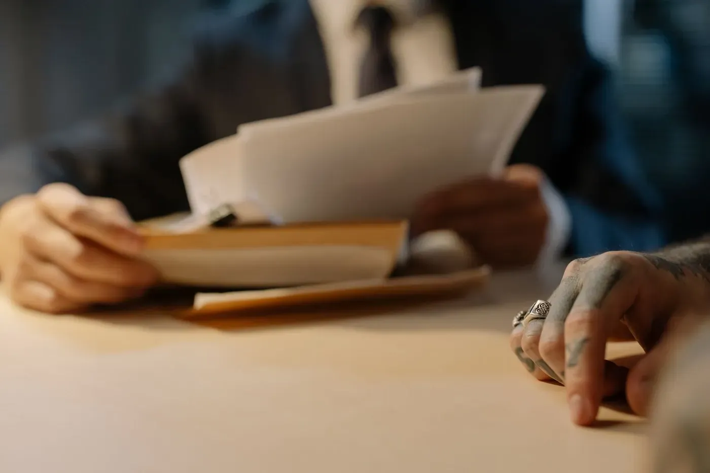 Hands holding a sheaf of papers across a desk from a second person.