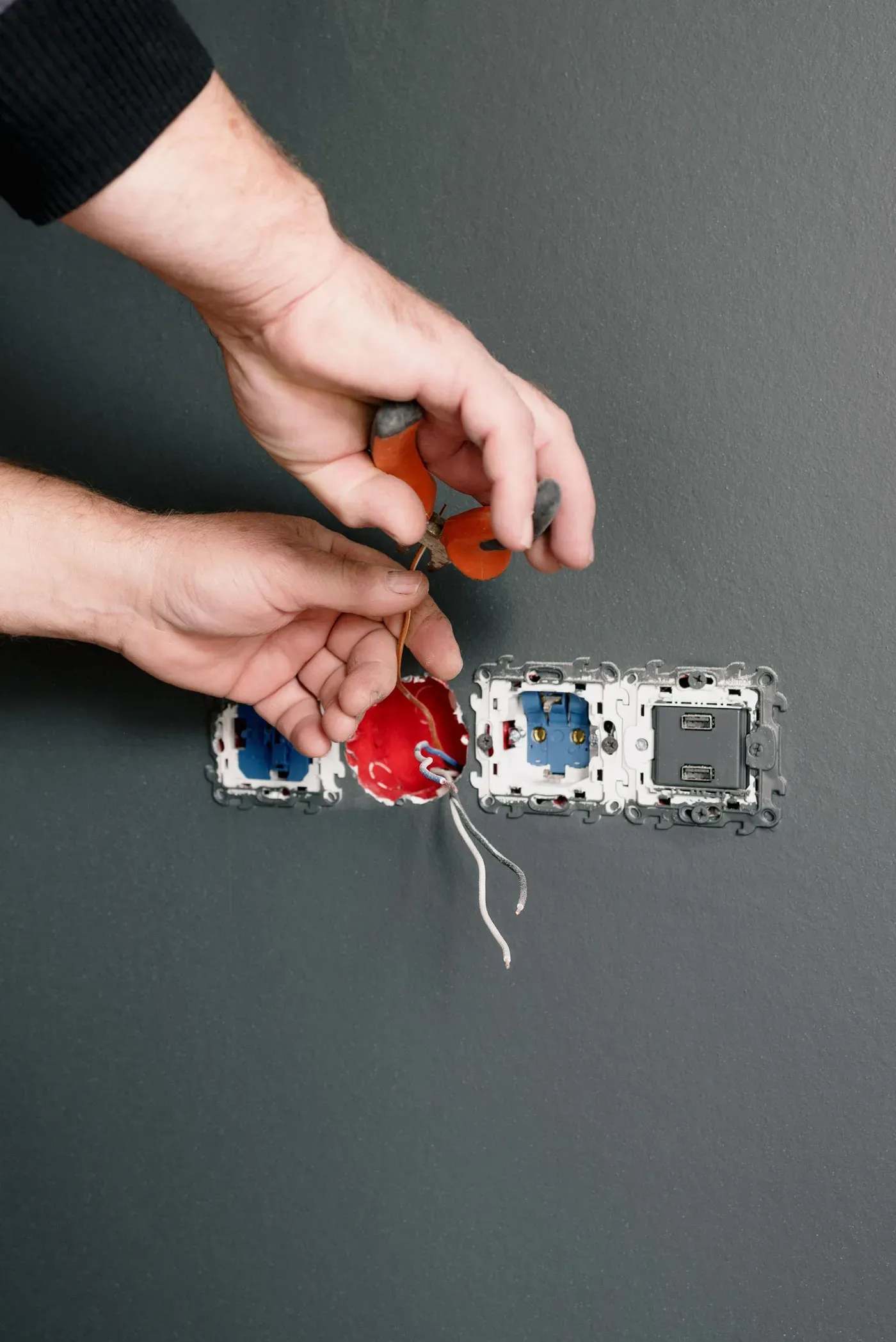 An electrician's hands wiring a wall socket.