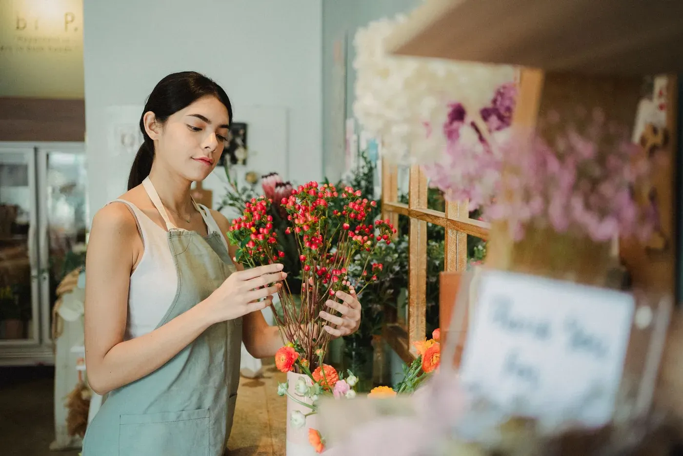A florist in an apron arranging red flowers in her shop.