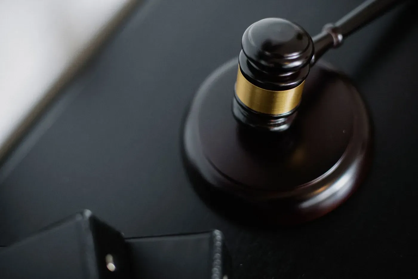A wooden gavel resting on its block on a dark desk beside a folder.
