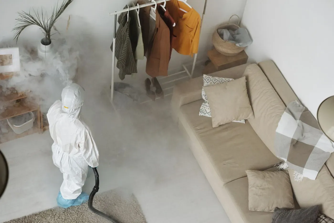 A worker in a white protective suit treating a living room with a fogging machine.