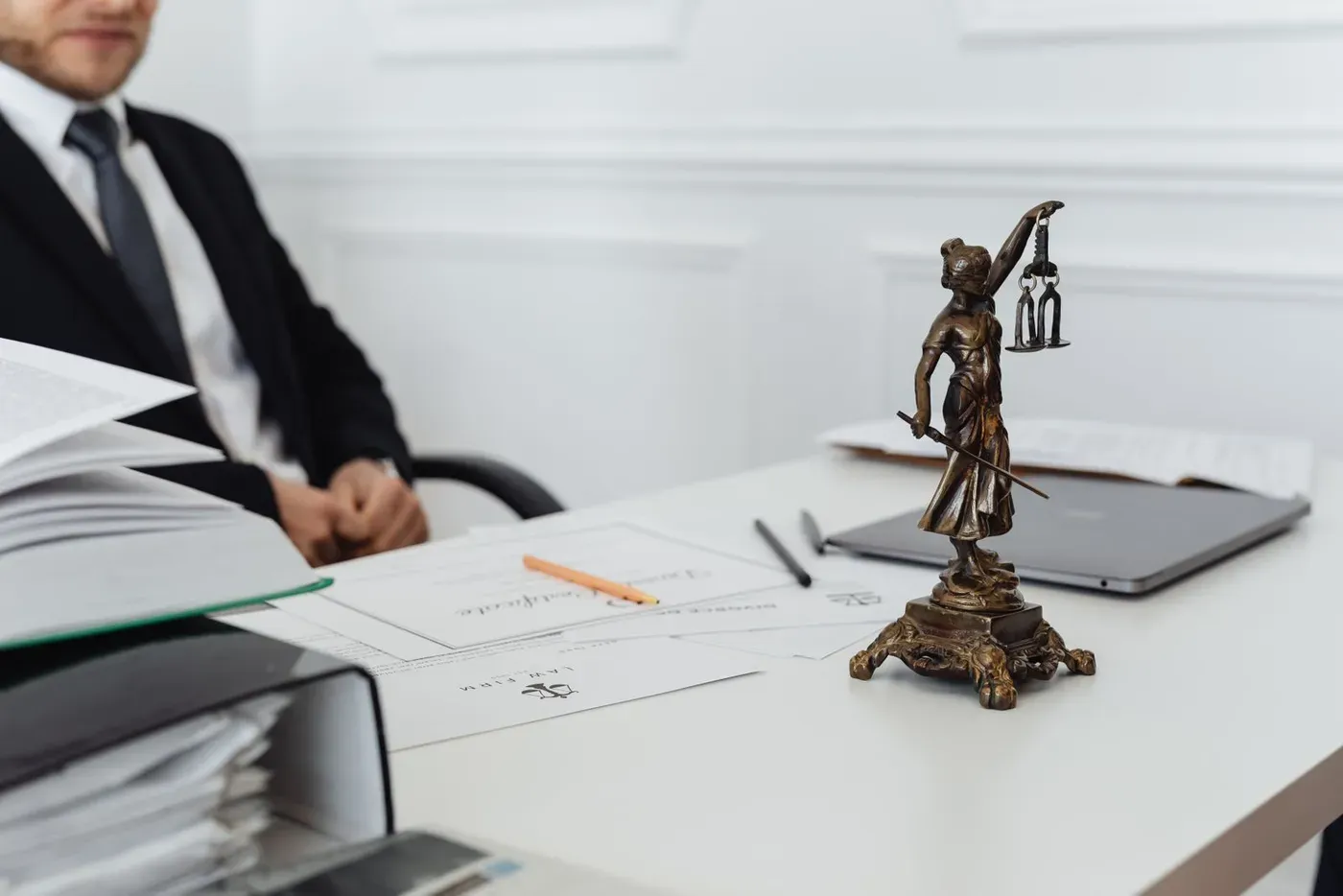 A desk in a law office with papers, a closed laptop and a small statue of Lady Justice.