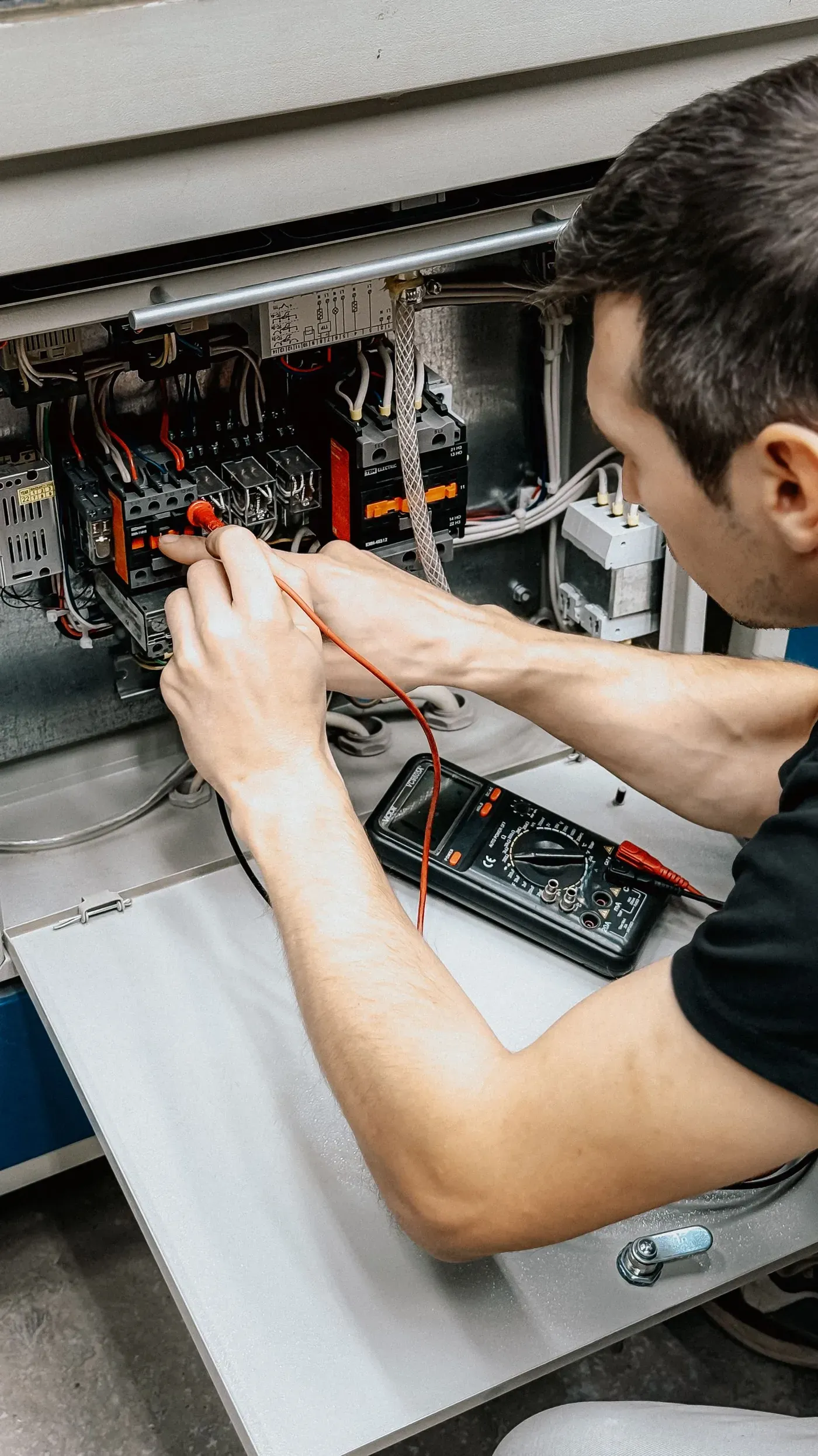 An electrician testing the connections in an open control panel with a multimeter probe.