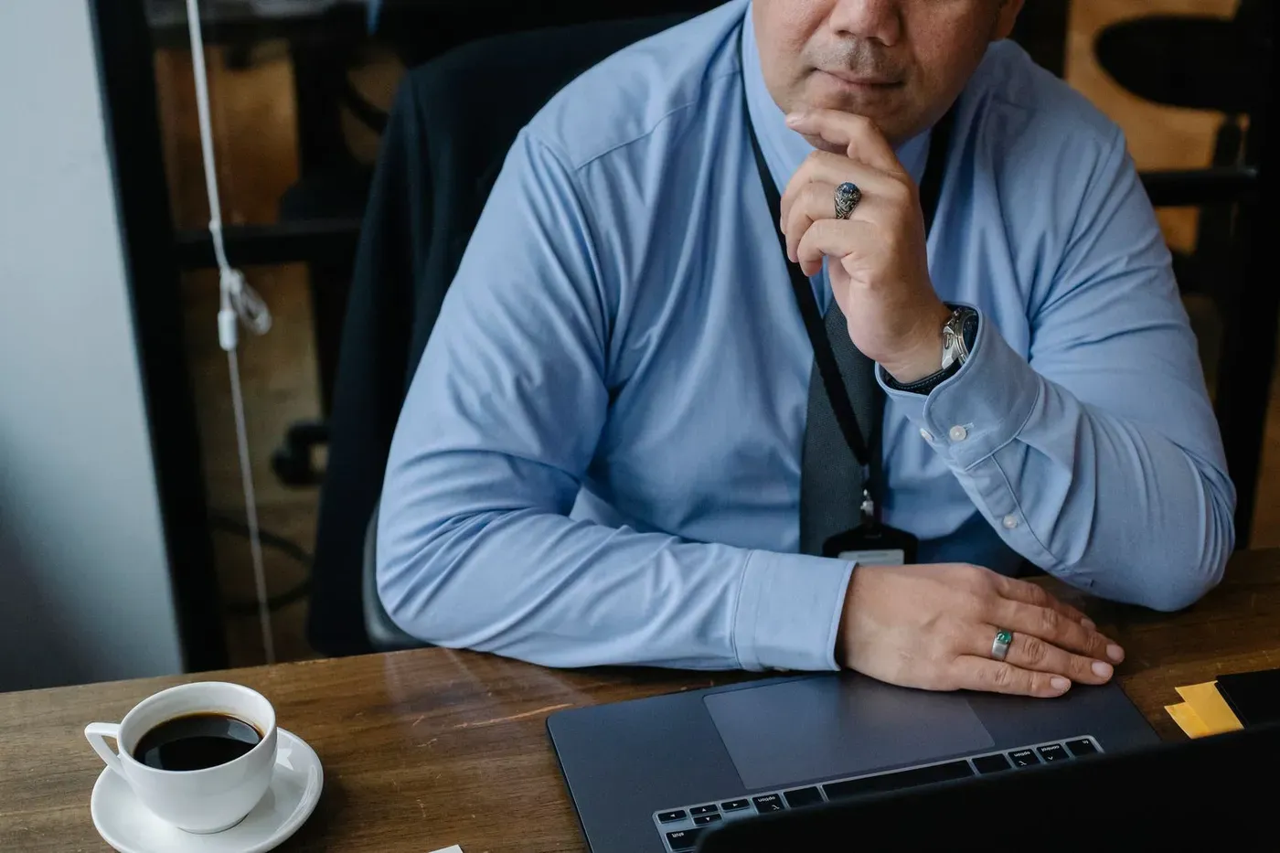 A business owner at his desk, hand on his chin, thinking while looking at his laptop.