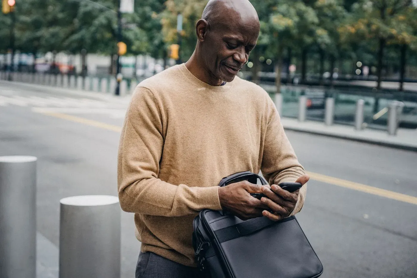 A man standing on a city street reading something on his phone.