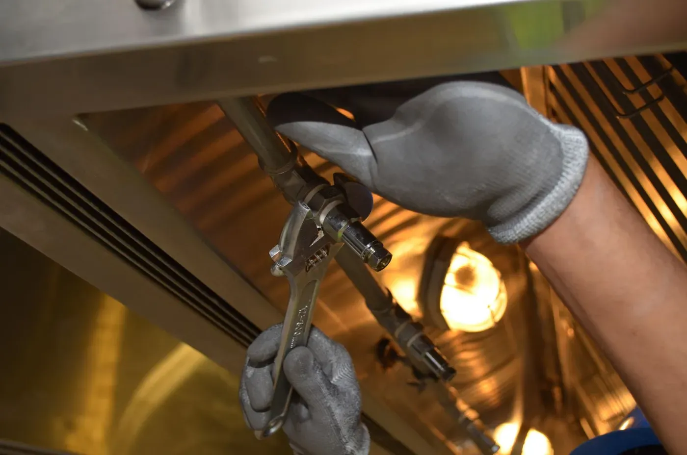 Gloved hands tightening a pipe fitting with an adjustable wrench.