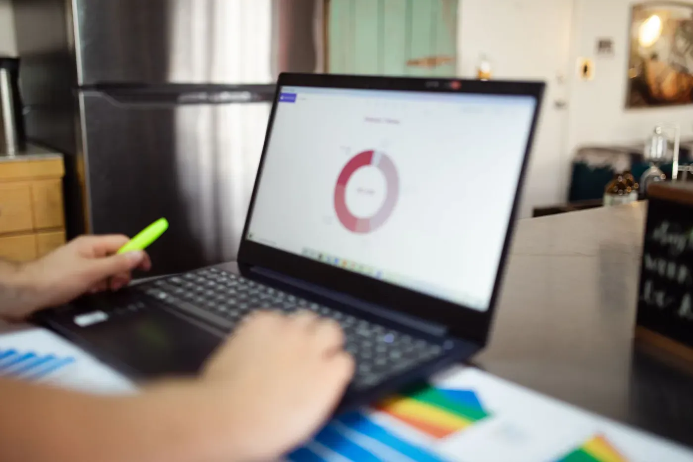 A person reviewing a pie chart on a laptop with a highlighter in hand and printed charts on the desk.