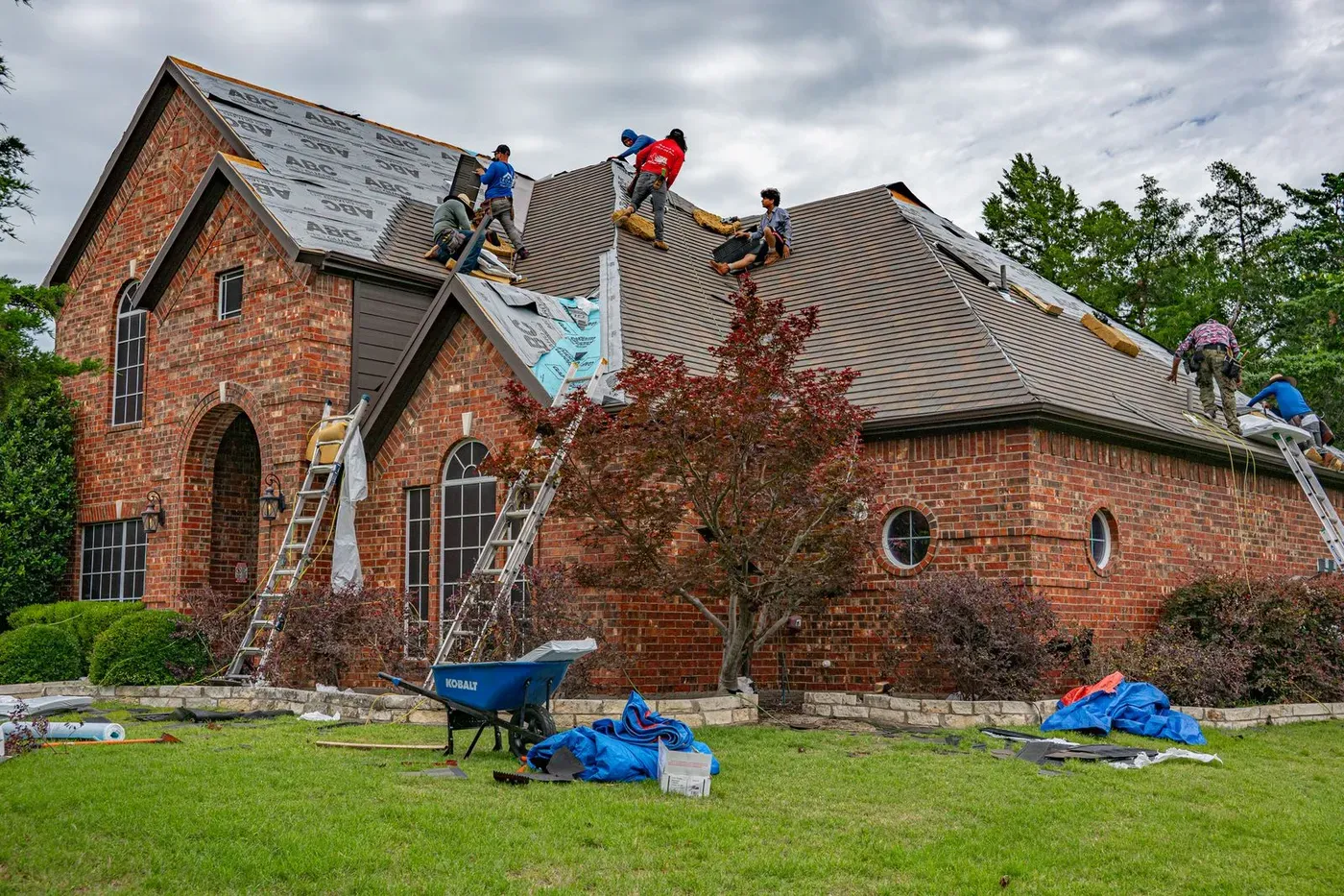 Roofers replacing the roof of a brick house in Allen, Texas, with ladders against the wall.