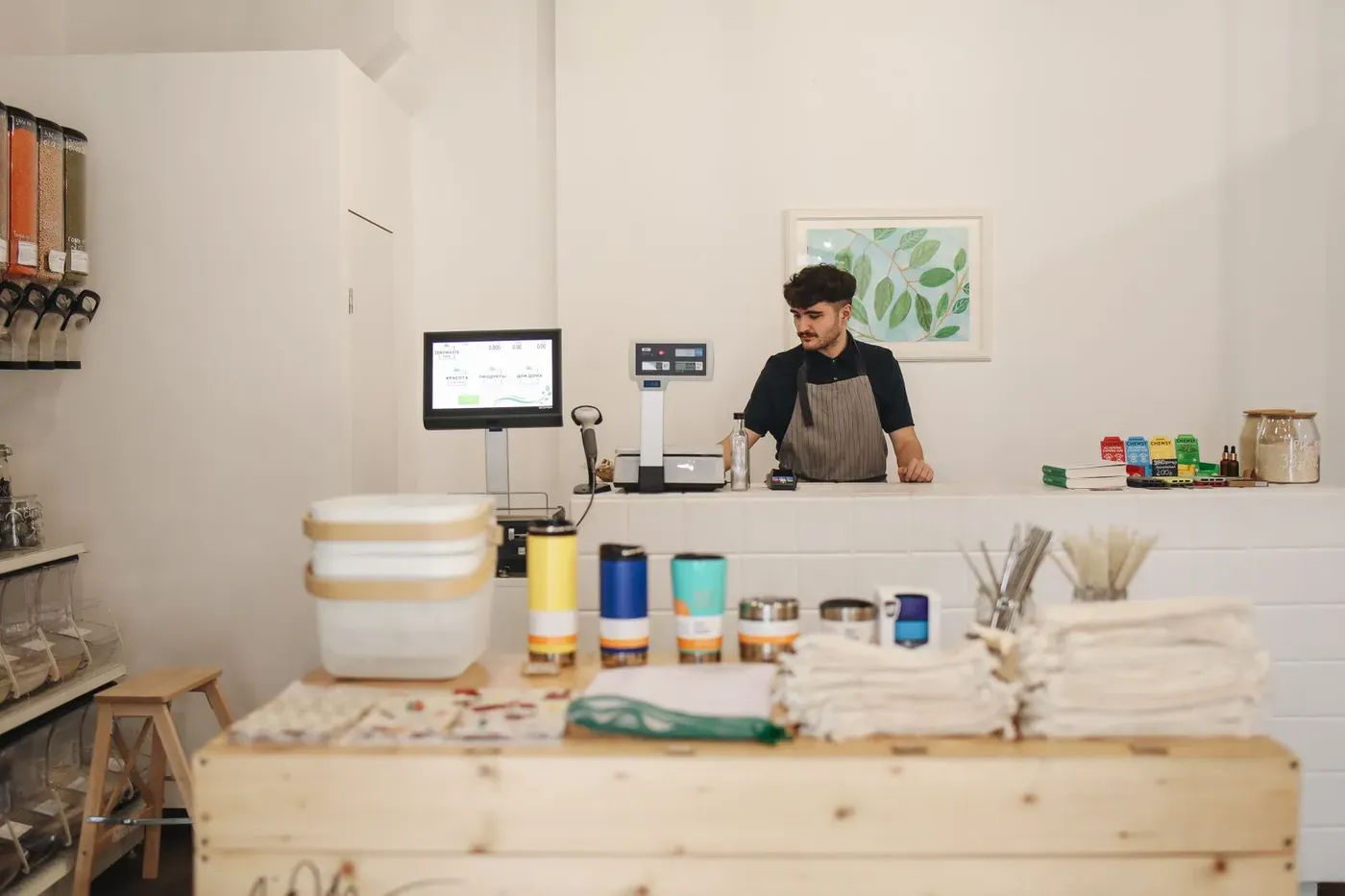 A young man standing behind the counter of a small refill shop.