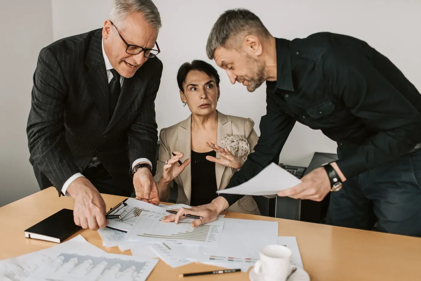Three colleagues leaning over printed charts on a meeting table.