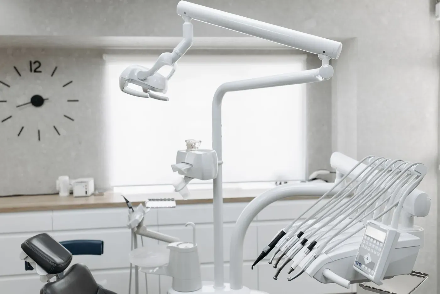 An empty dental treatment room with an overhead lamp and a tray of handpieces.