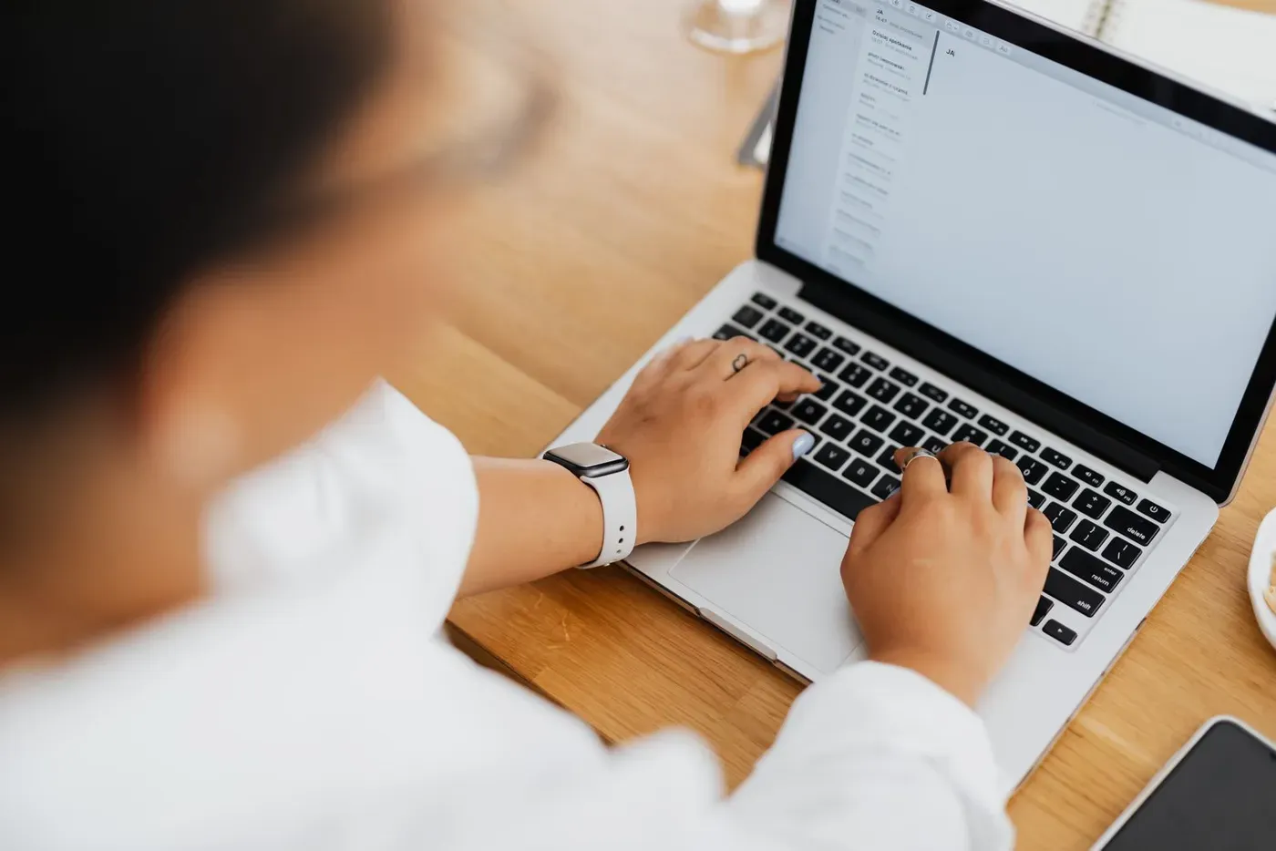 A person typing on a laptop at a wooden desk.
