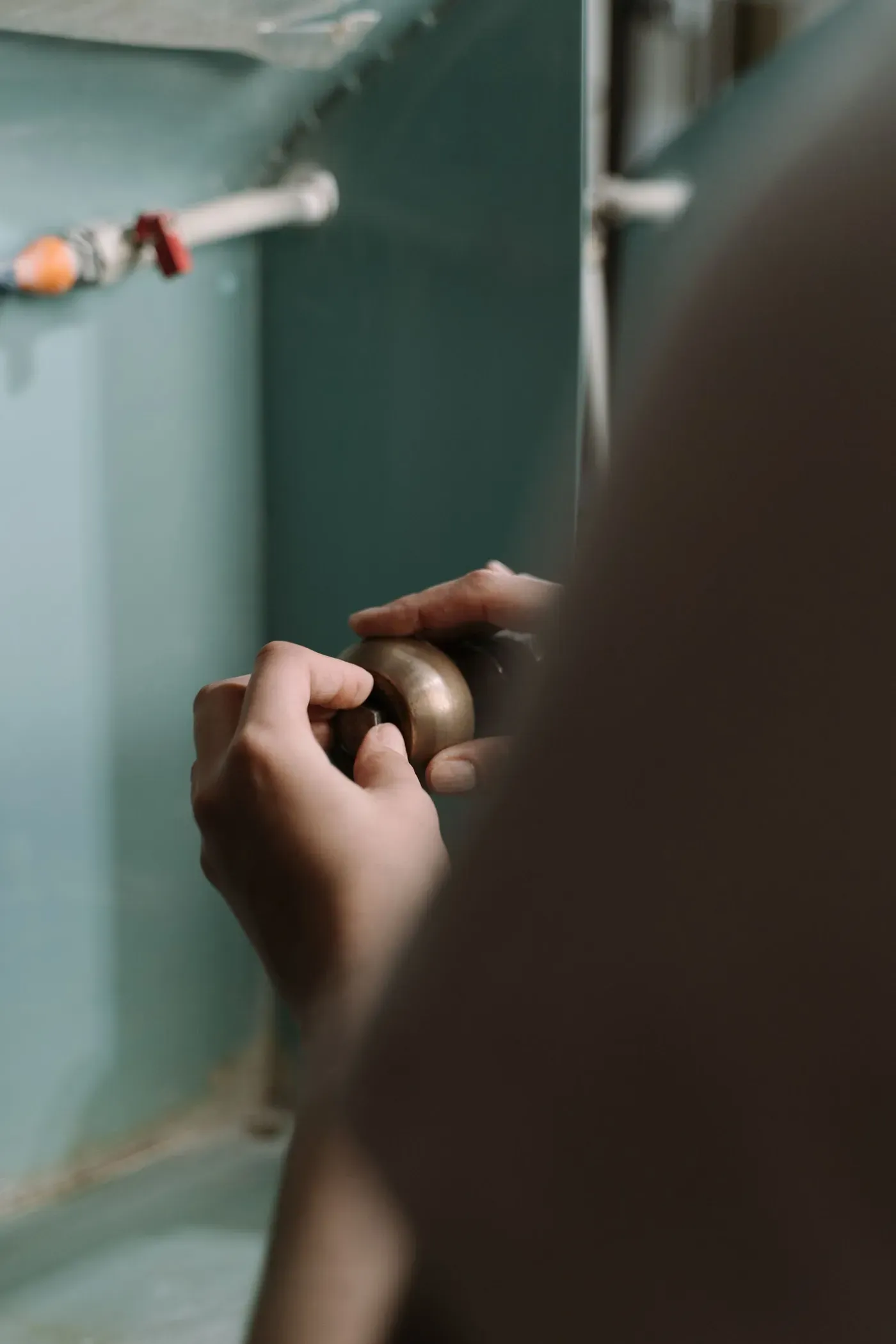 Two hands tightening a brass pipe fitting in the cabinet under a sink.